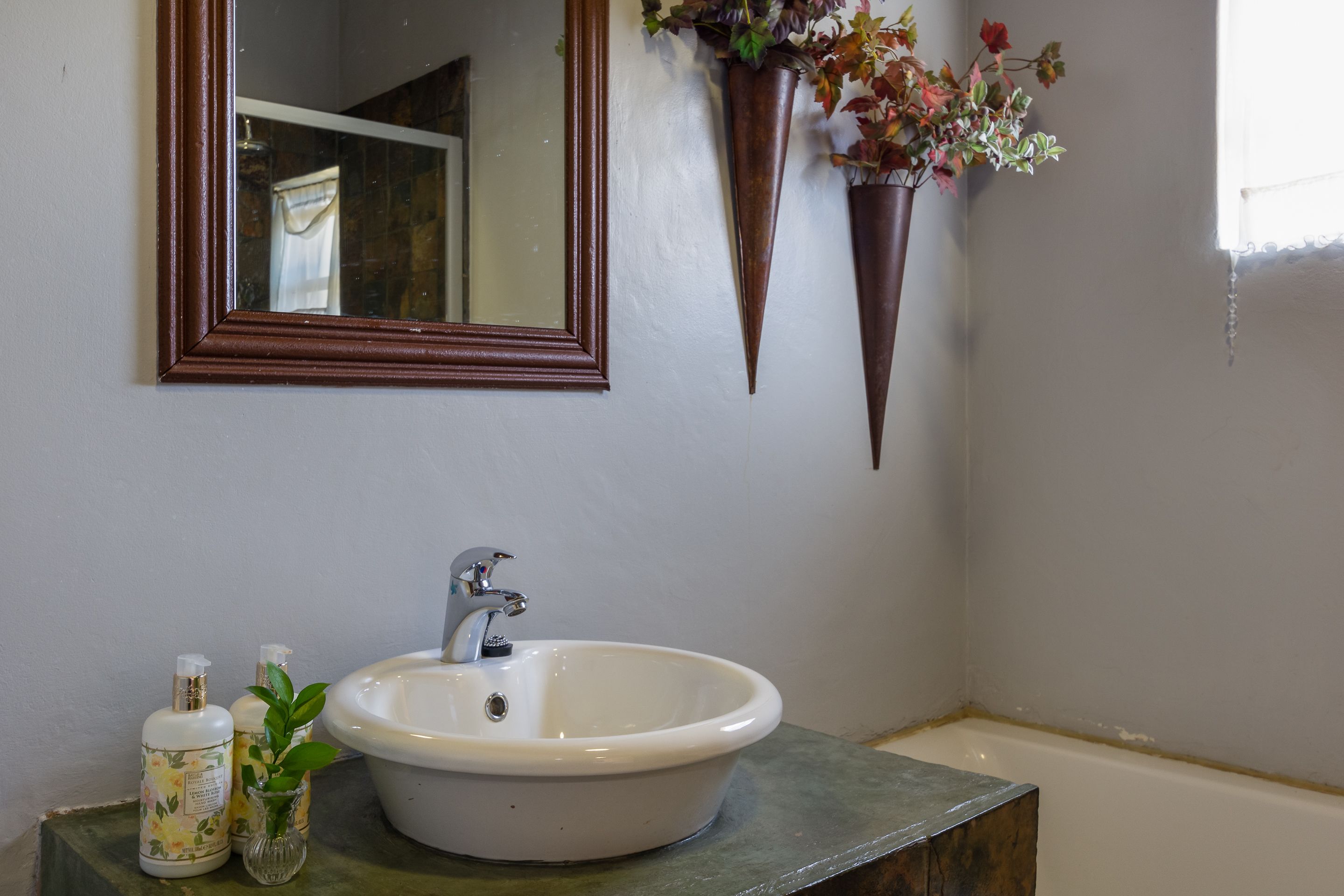 A bathroom with a white sink, a mirror, and two flower pots on the wall.