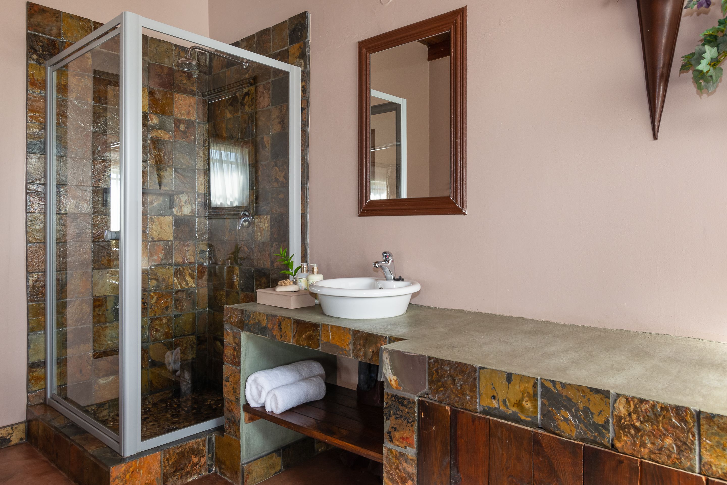 Een badkamer met een douche met glazen wand, een witte wastafel en een spiegel.