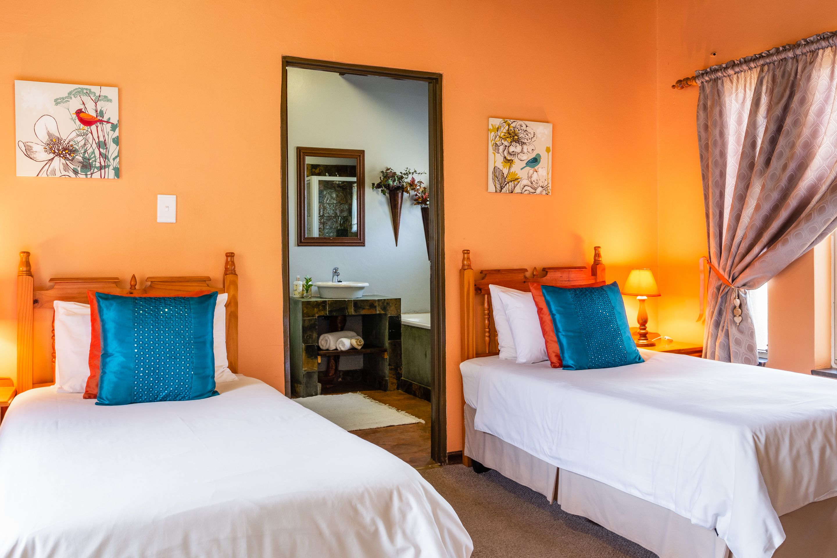 Habitación de hotel con dos camas, un espejo, obras de arte en las paredes y un baño visible a través de una puerta abierta.