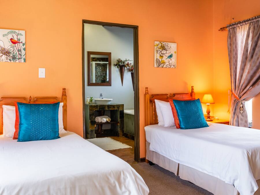 Habitación de hotel con dos camas, un espejo, obras de arte en las paredes y un baño visible a través de una puerta abierta.
