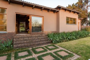 A house with a brick foundation, a wooden deck, and a garden with green plants and a patterned lawn. - Aberfeldy Bed and Breakfast (Midrand)