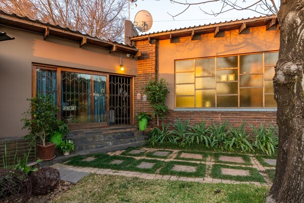 A house with a brick exterior, large windows, and a well-maintained garden with potted plants and a stone pathway. - Aberfeldy Bed and Breakfast (Midrand)
