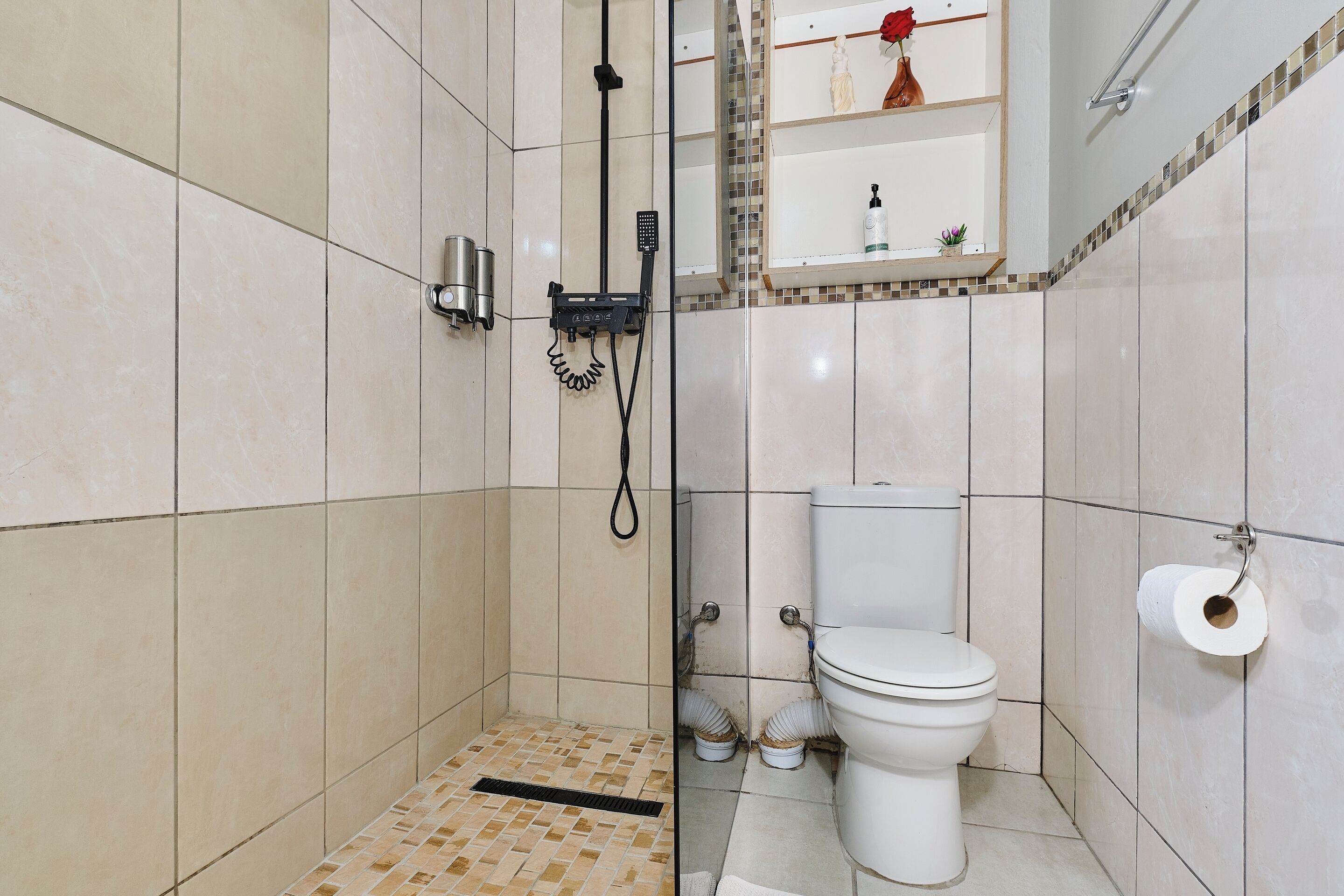 A bathroom with a shower, toilet, and a shelf with toiletries.