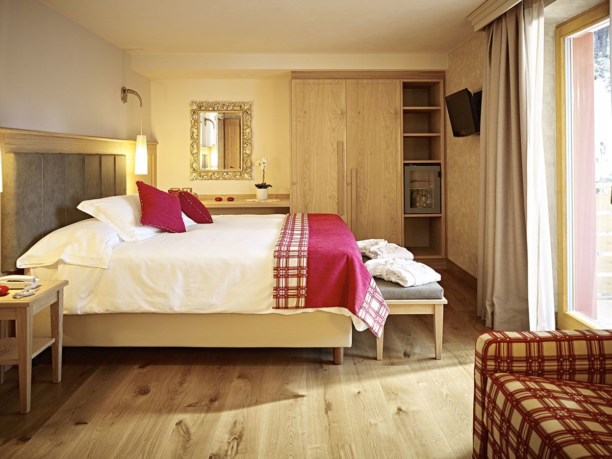 A hotel room with a large bed, bedside tables, a wardrobe, a television, and a window with curtains.