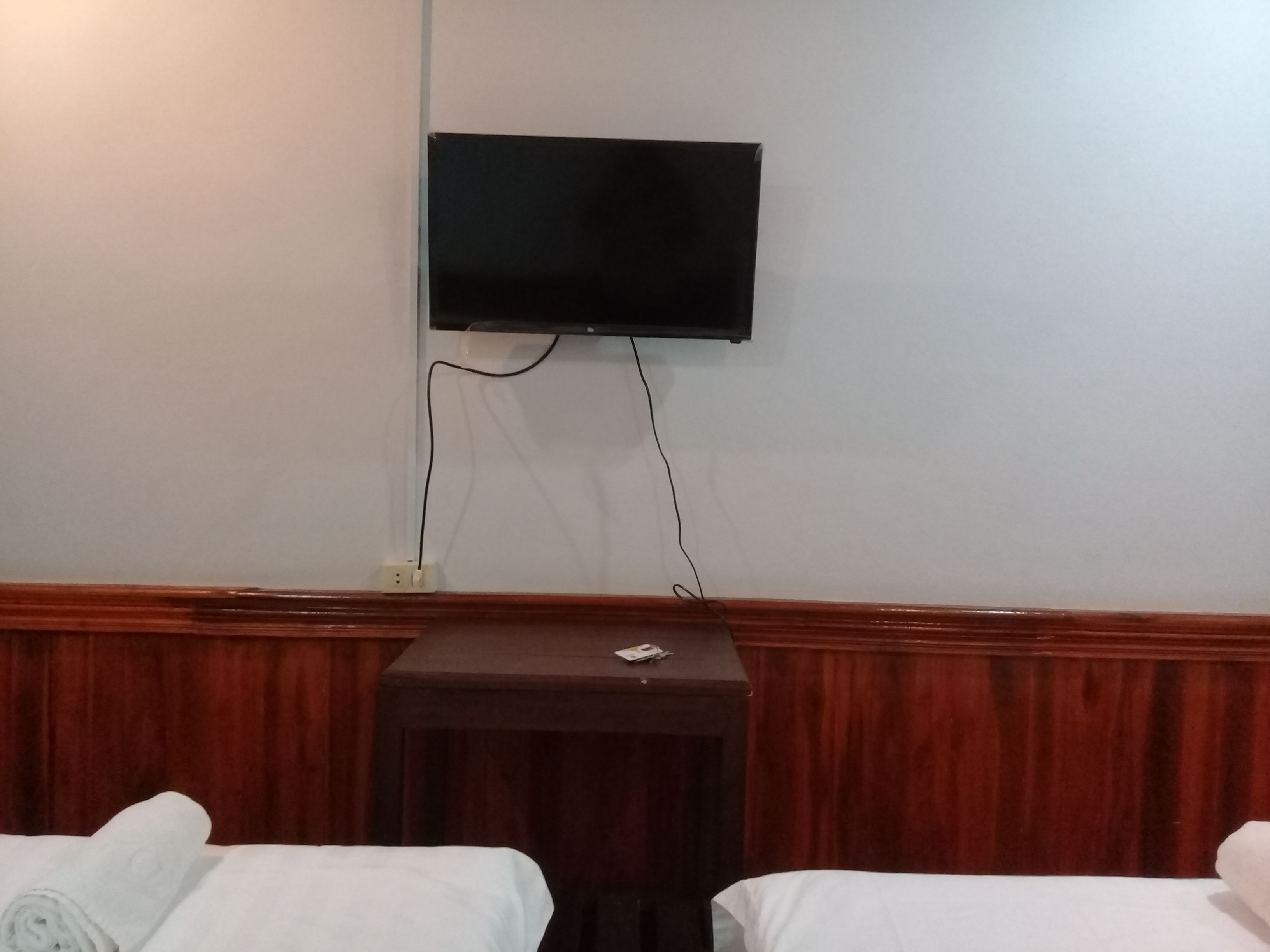 Una camera d'albergo con due letti, un piccolo tavolino, una TV a parete e una presa elettrica.