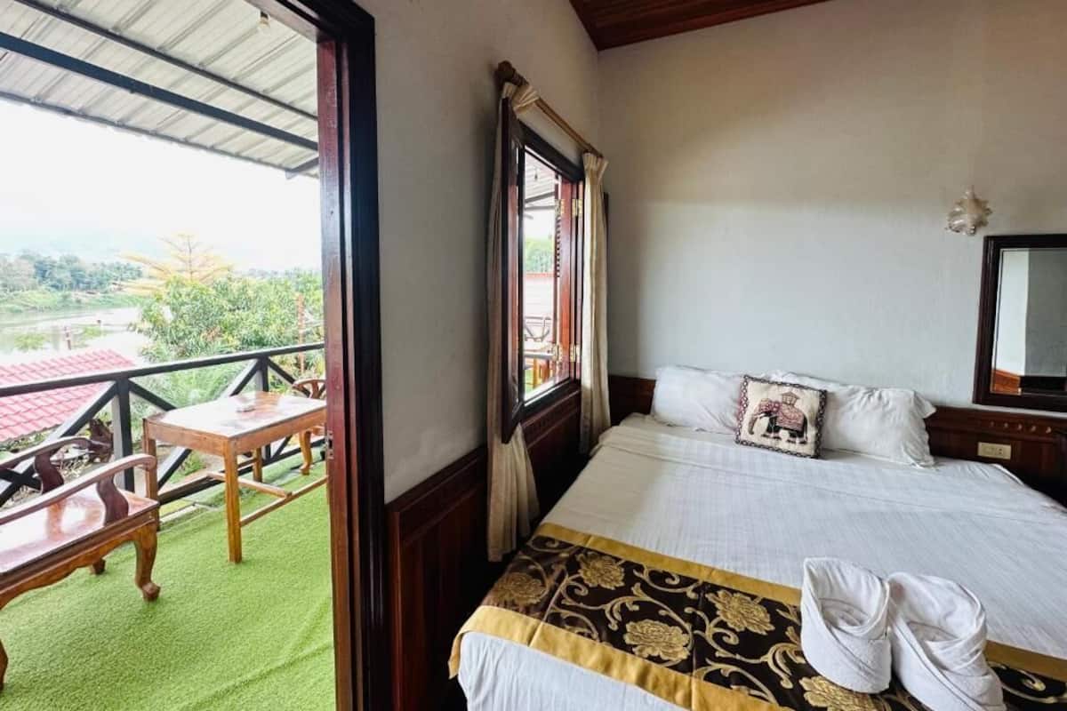 A hotel room with a bed, a balcony with a table and chairs, and a view of the outdoors.