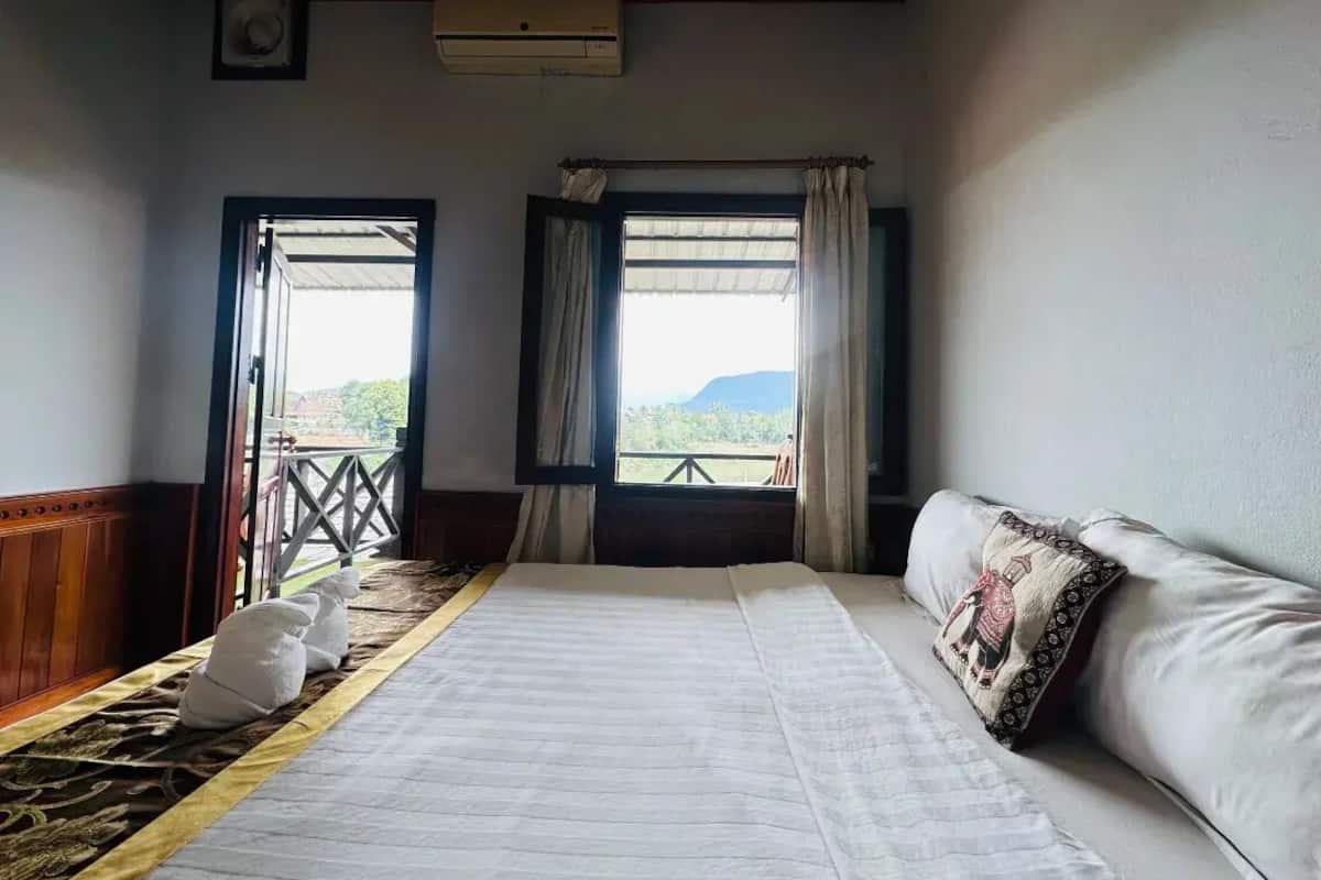 A hotel room with a bed, two windows with curtains, a balcony, and a view of the outdoors.