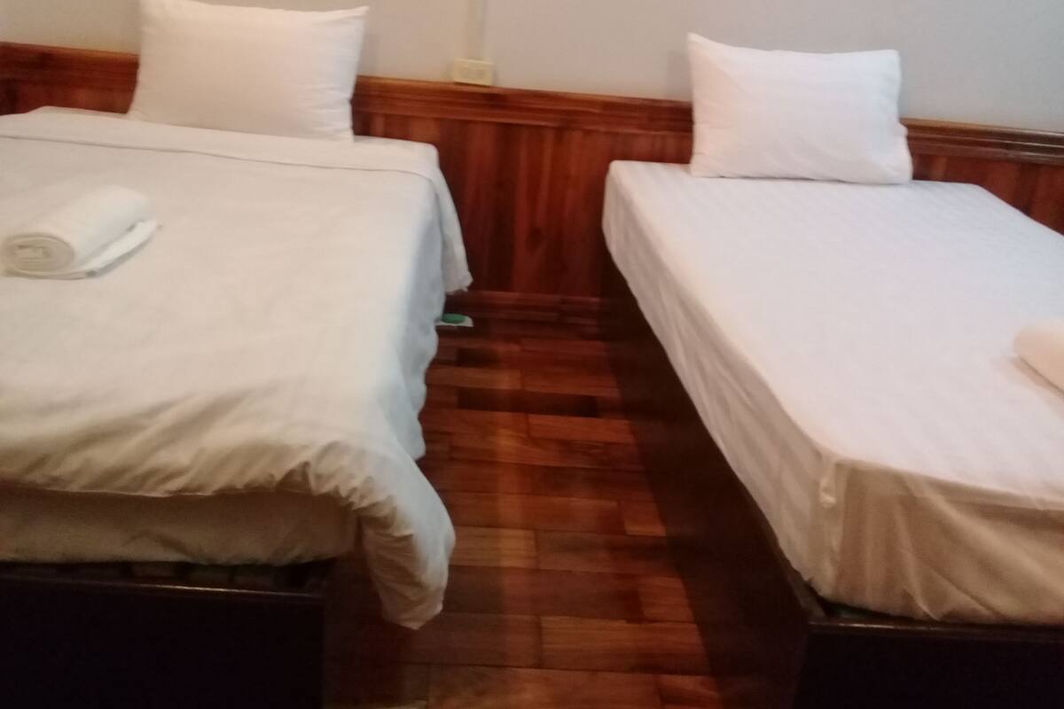 Two single beds with white linens, a wooden floor, and a wooden headboard.