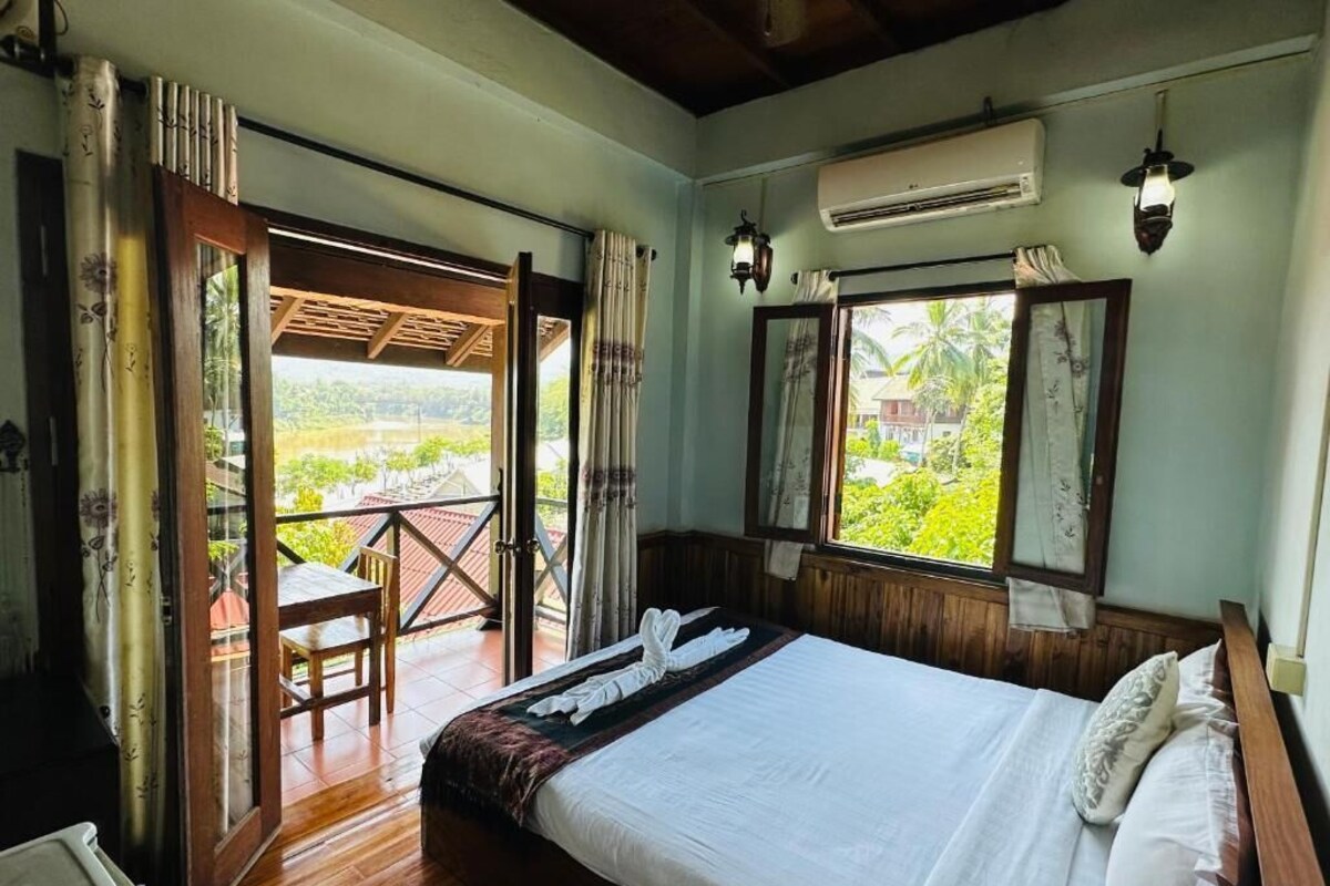 Un dormitorio con cama, ventana, aire acondicionado y balcón con mesa y silla.
