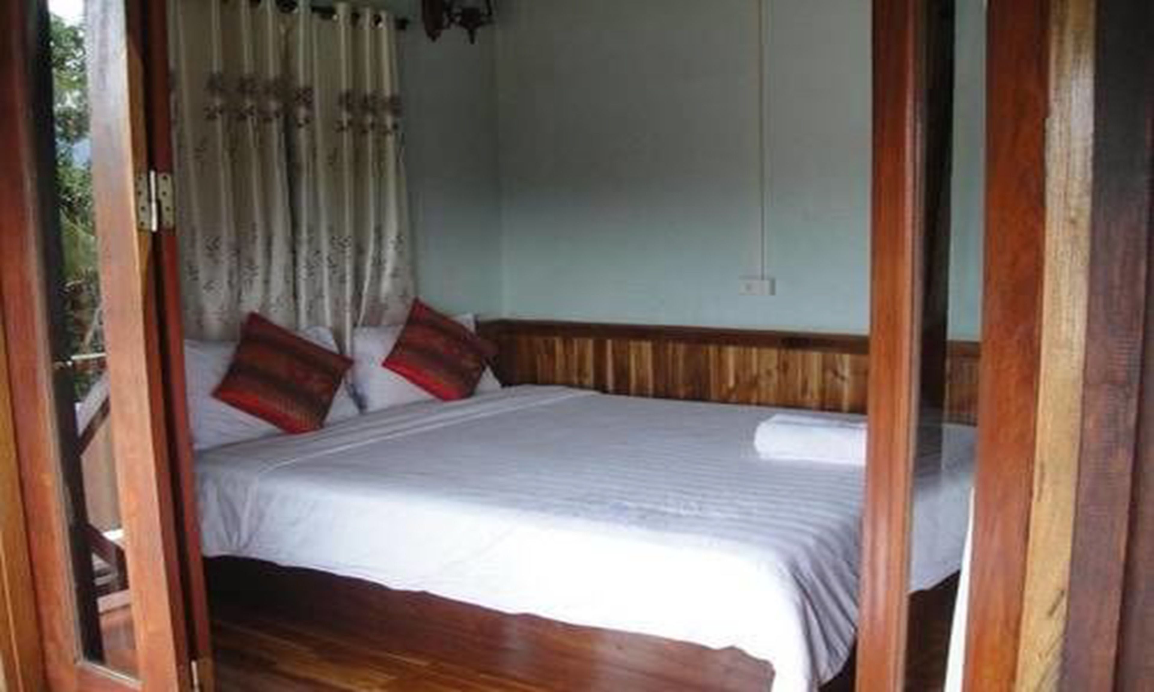 Een slaapkamer met een houten bedframe, witte beddengoed en twee rode kussens.