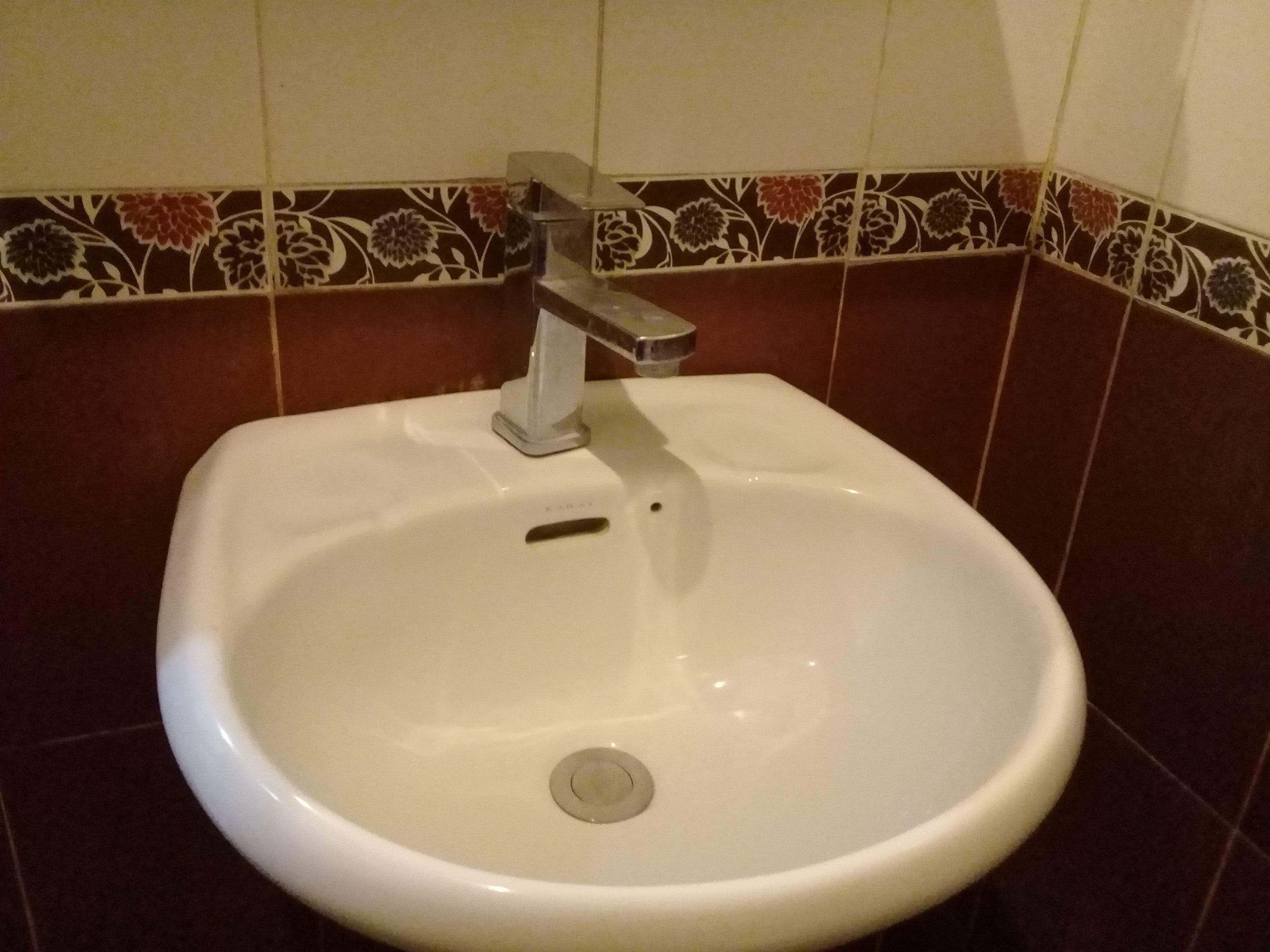 A white bathroom sink with a silver faucet, set against a wall with patterned tiles.