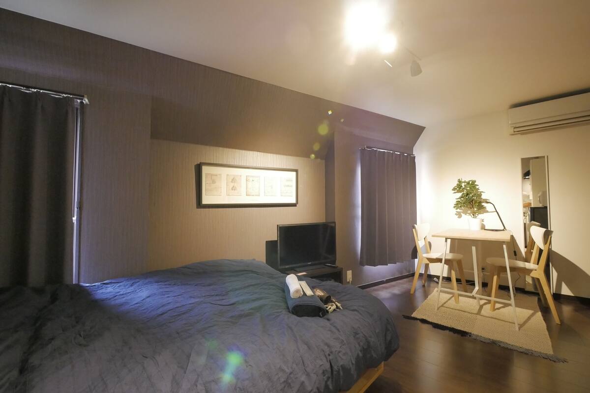 A hotel room with a bed, a desk with a chair, a television, and a potted plant.