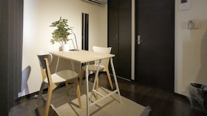 A small, modern room with a wooden table and chairs, a potted plant, a dark door, and an air conditioning unit on the wall. - Apartment Sun Bright (Tokyo)