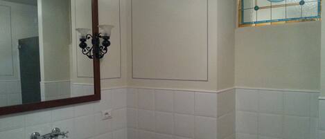 Un baño con paredes de azulejos blancos, un espejo grande, un lavabo y un ventanal con vidrieras de colores.