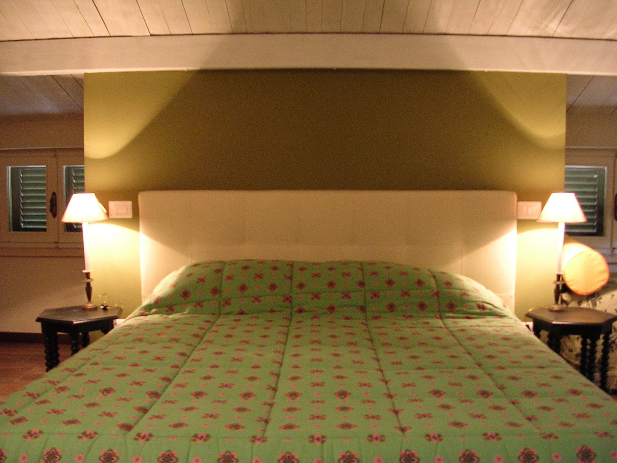 A bedroom with a green floral bedspread, two bedside lamps, and a wooden headboard.