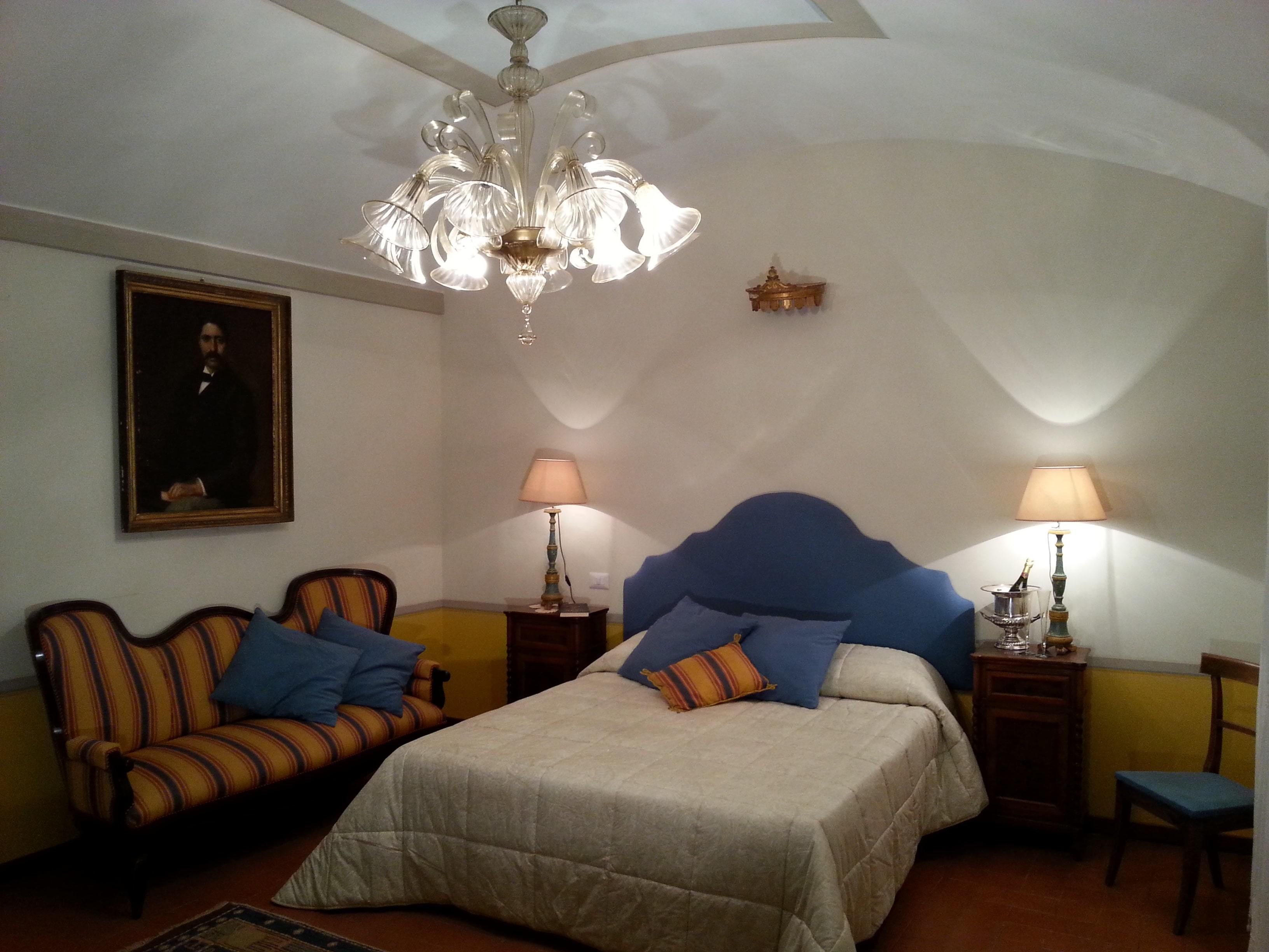 Una camera da letto con un letto, una poltrona, un divano, due comodini, un lampadario e un quadro appeso al muro.