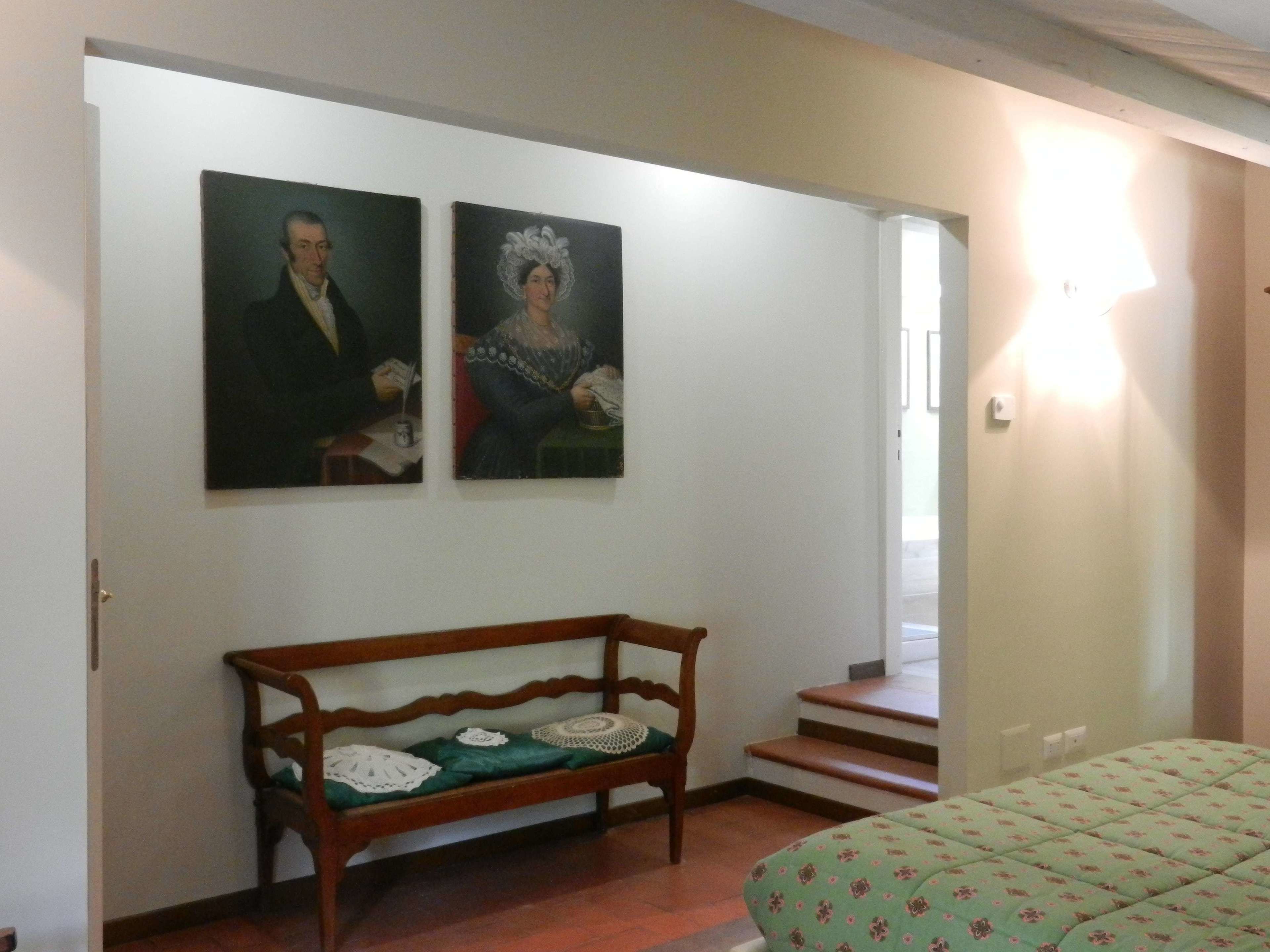 Une pièce avec un banc en bois, un lit recouvert d’une courtepointe à motifs et deux tableaux accrochés au mur.