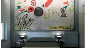 Un dormitorio con una cama, dos mesitas de noche y una pared grande con grafitis y dibujos.