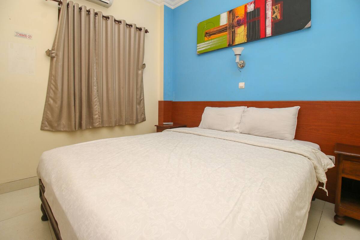 A bedroom with a bed, curtains, a nightstand, and a wall-mounted light fixture.