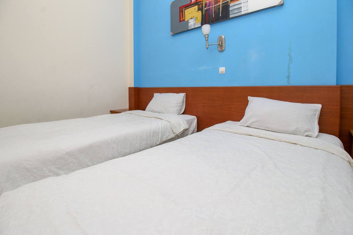 A hotel room with two single beds, a blue accent wall, and a wall-mounted light fixture.