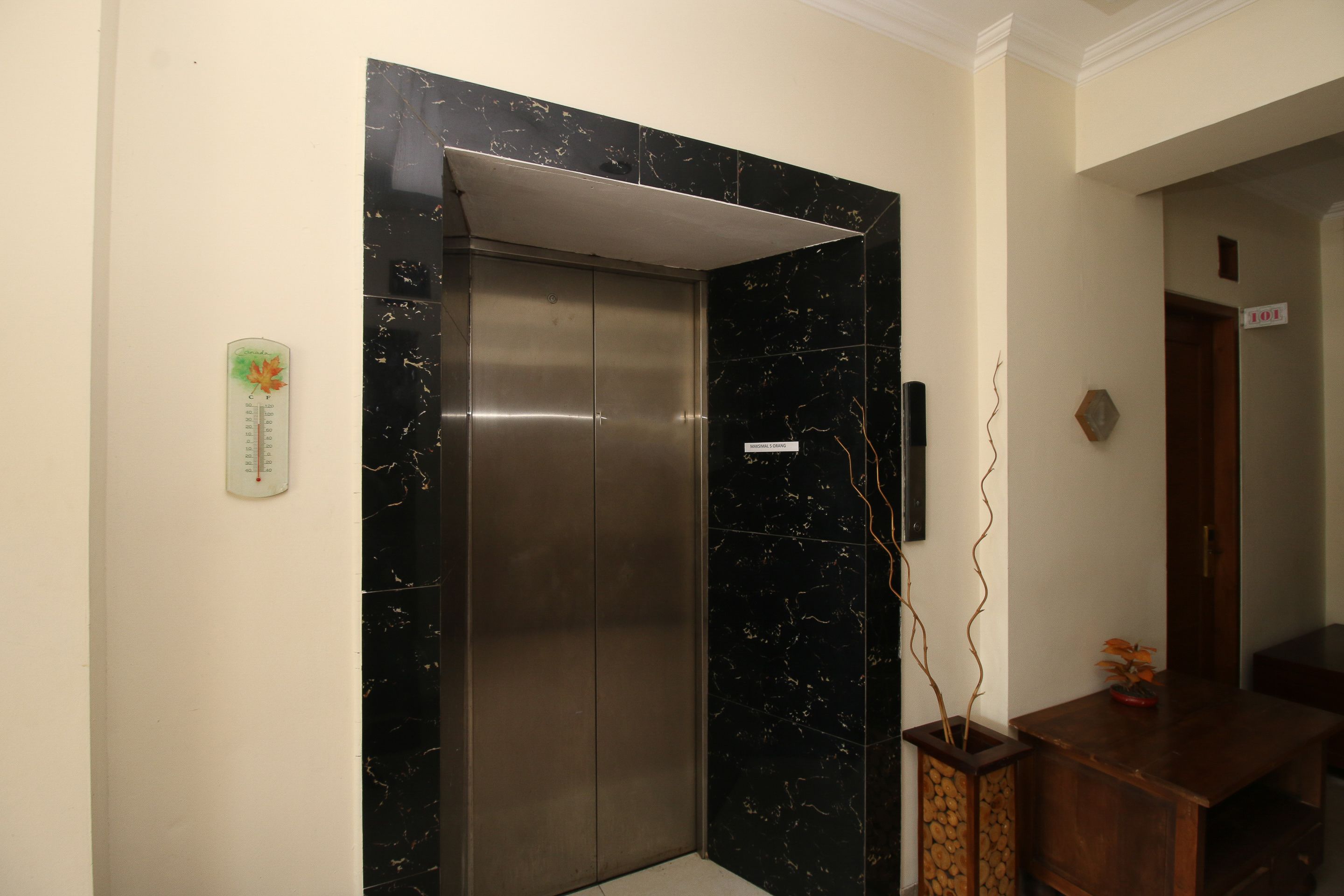 A modern elevator with a marble finish, a temperature control device on the wall, and a wooden desk with a vase.