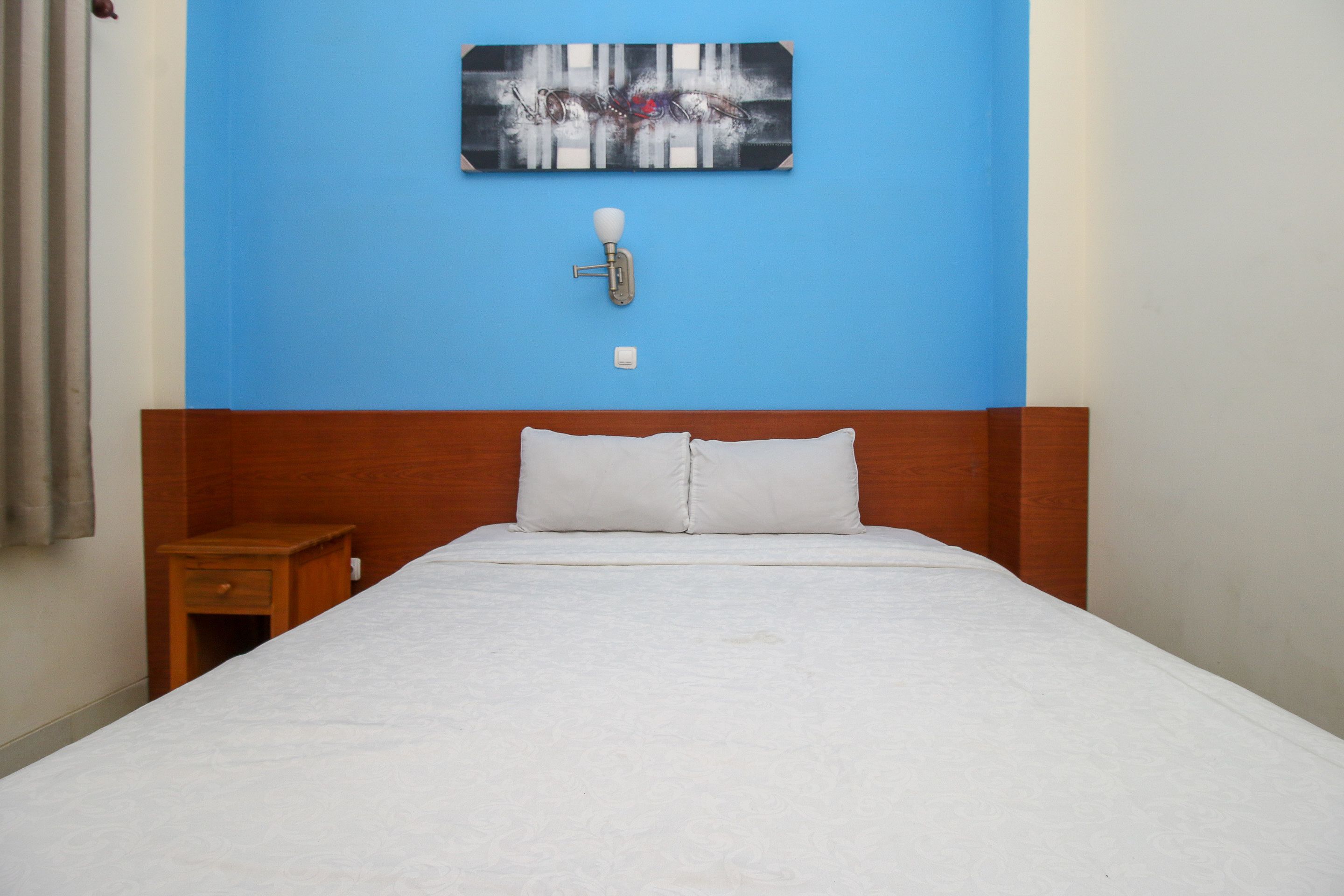 Una habitación de hotel con una cama grande, cabecero de madera, una mesita de noche, una lámpara de pared y un cuadro sobre la cama.