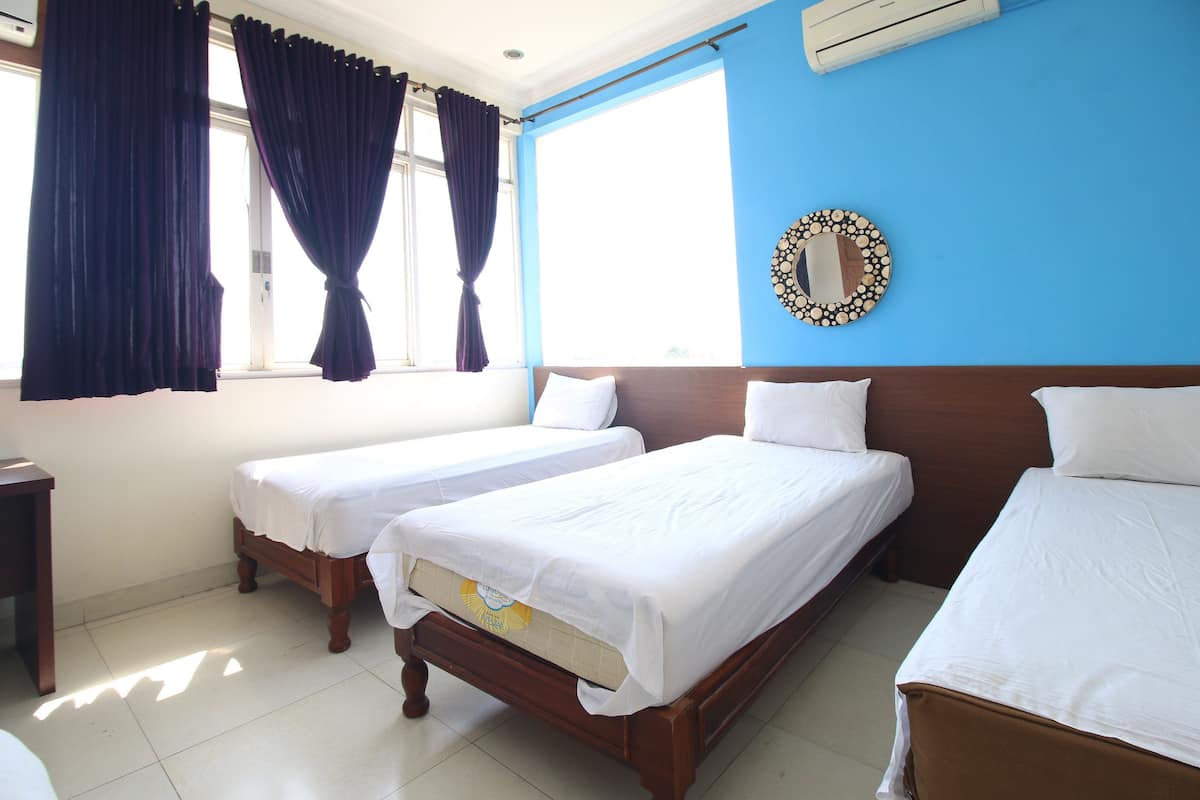 A hotel room with two single beds, a wooden headboard, a large mirror, and a window with curtains.