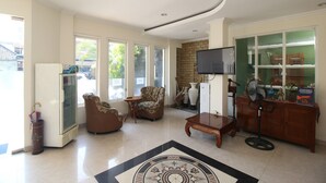 A spacious living room with a large window, a fireplace, a television, and a cabinet with decorative items. - Hotel Vala Malioboro Yogyakarta (Yogyakarta)