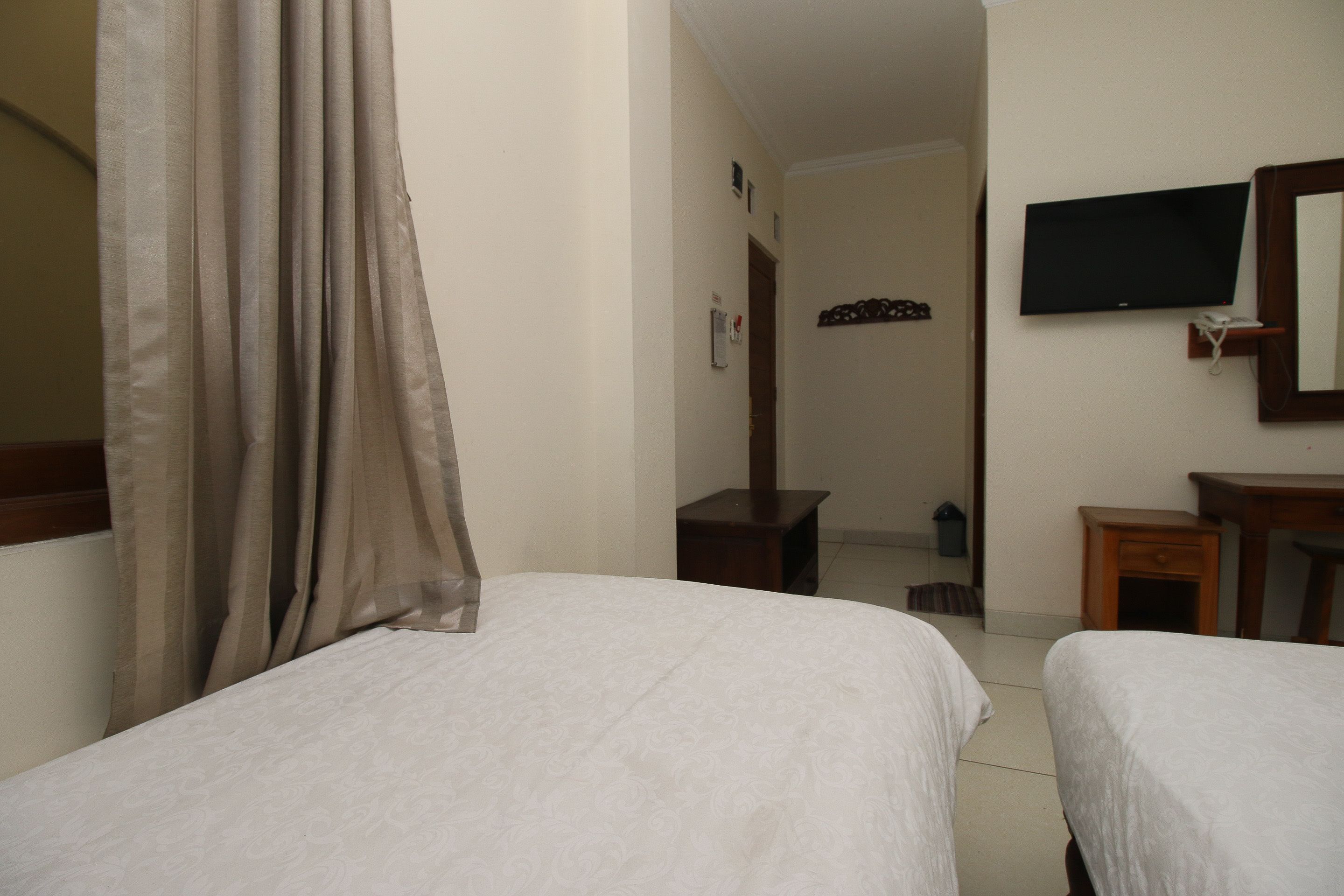 A hotel room with two beds, a television mounted on the wall, a small wooden nightstand, and a mirror.