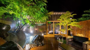 Un espacio de estar al aire libre en estilo japonés tradicional, con suelo de madera, rocas grandes y un elemento acuático.