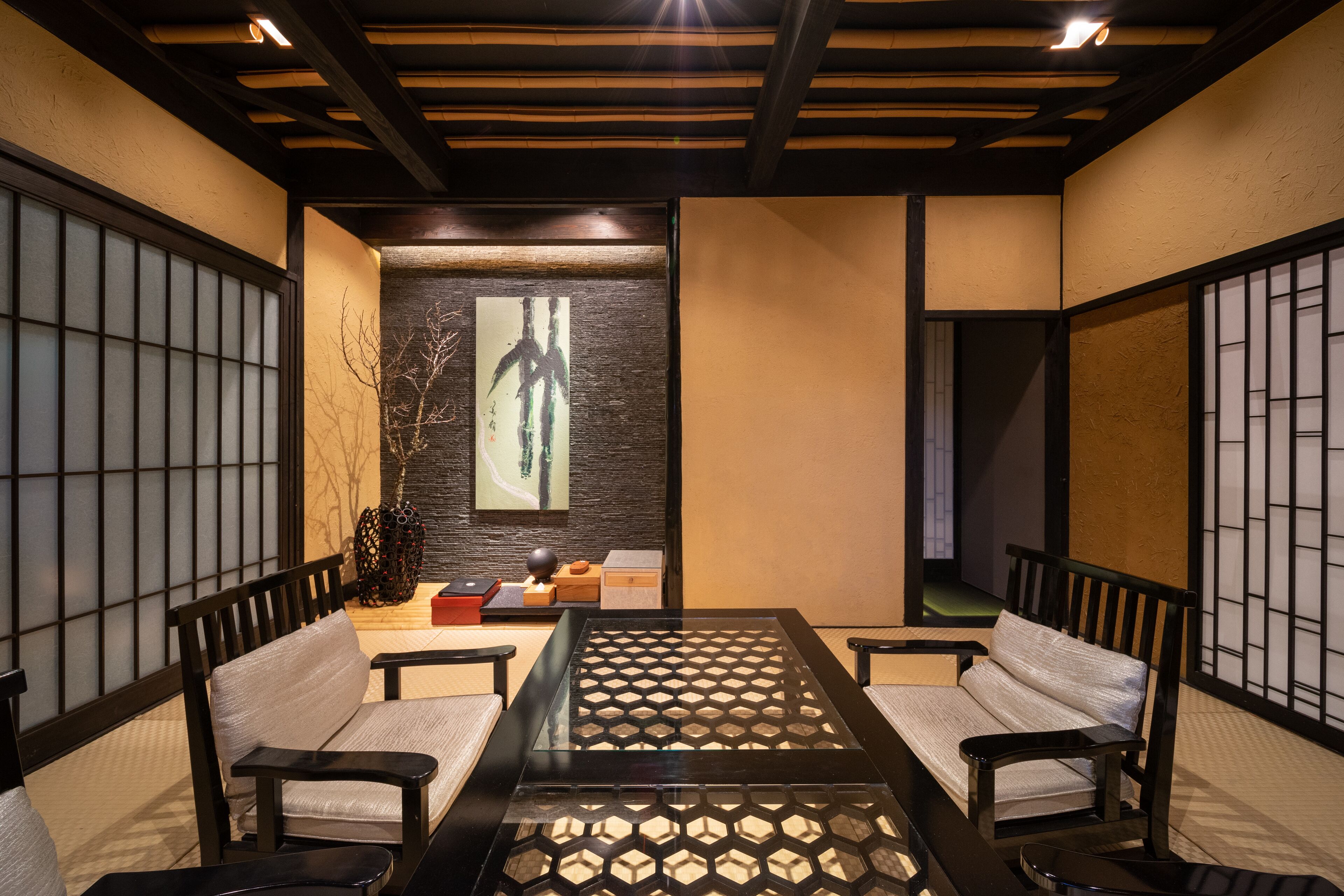 A traditional Japanese-style room with tatami flooring, a low table with a geometric glass top, and shoji screens on the walls.