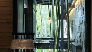 Una habitación con separador de vidrio, plantas de bambú, pared de piedra y un banco de madera.
