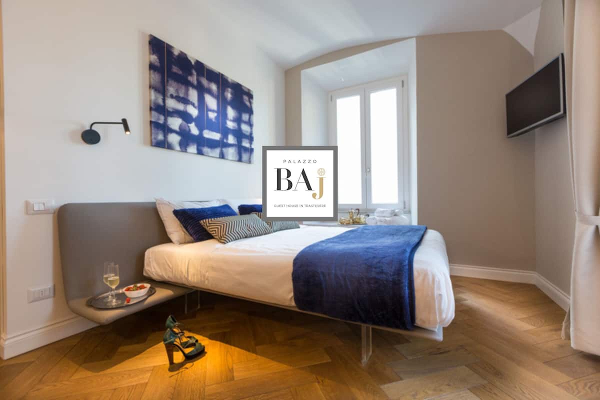 A modern guest room with a bed, a small table with a glass of wine, and a TV mounted on the wall.