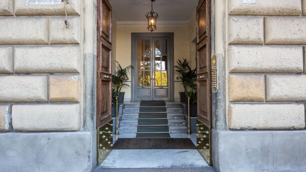 Une entrée d’immeuble avec une enseigne indiquant « Condominio », un escalier recouvert d’une moquette et un luminaire suspendu.