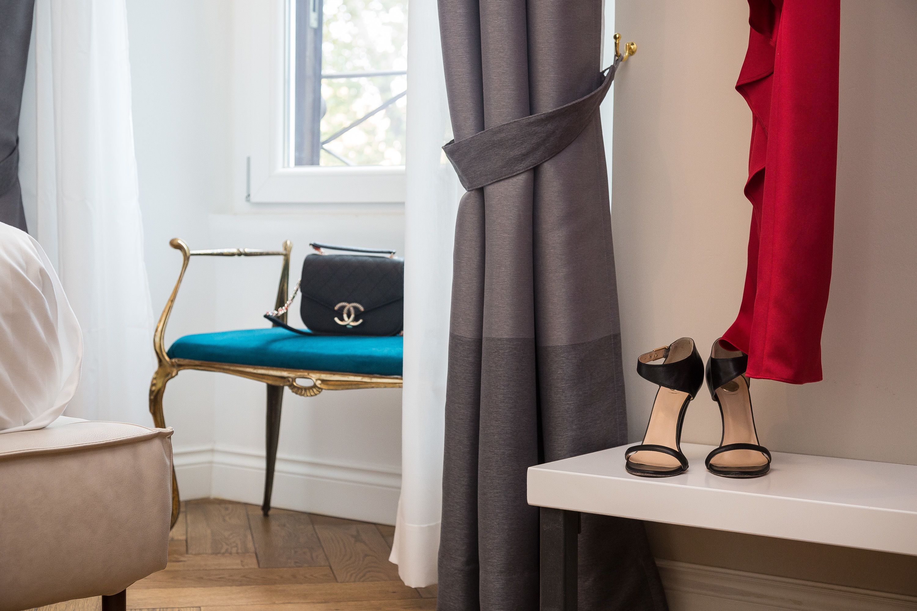 Ein Zimmer mit Stuhl, einer Bank, einem Paar schwarzer Sandalen auf einem Regal und einer Handtasche auf der Bank.