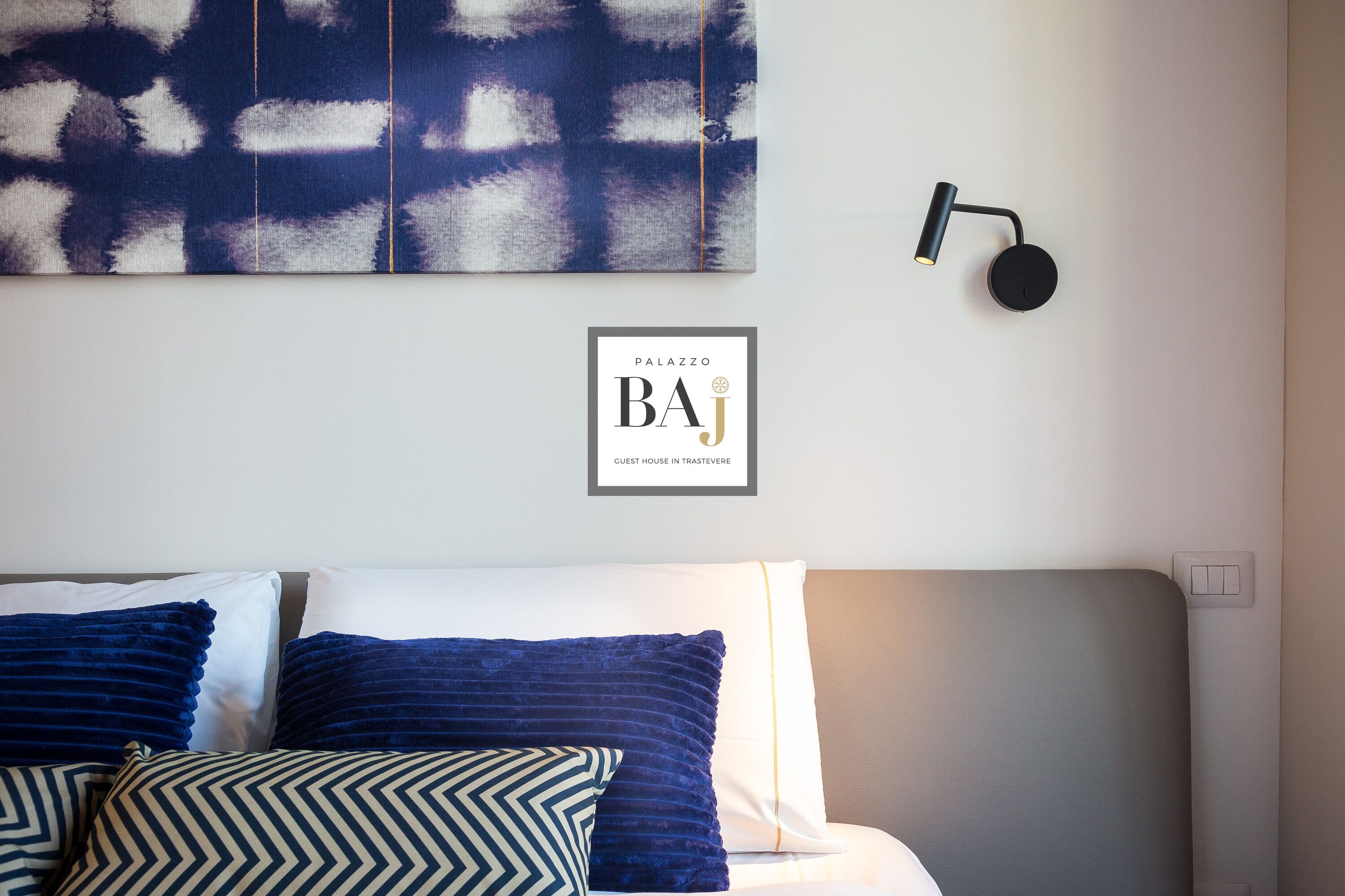 A neatly arranged bed with blue and white pillows, a wall-mounted light fixture, and a framed sign above the bed.