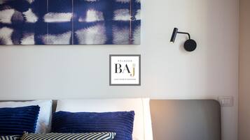 A neatly arranged bed with blue and white pillows, a wall-mounted light fixture, and a framed sign above the bed.