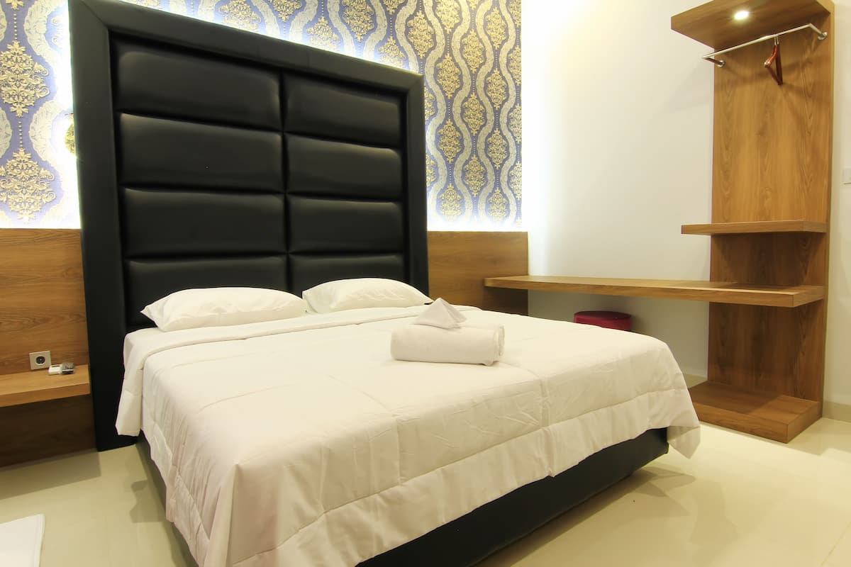 A neatly made bed with a black headboard, a wooden shelf unit, and a patterned wallpaper.