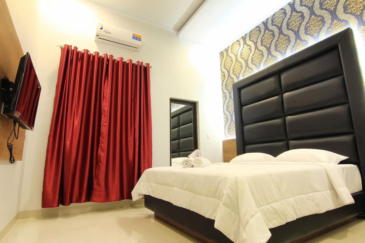 A hotel room with a large bed, red curtains, a mounted TV, and a patterned wall.