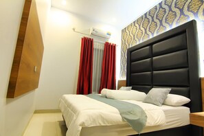 Une chambre d’hôtel avec un lit, un climatiseur fixé au mur, une fenêtre avec des rideaux rouges et un papier peint à motifs.