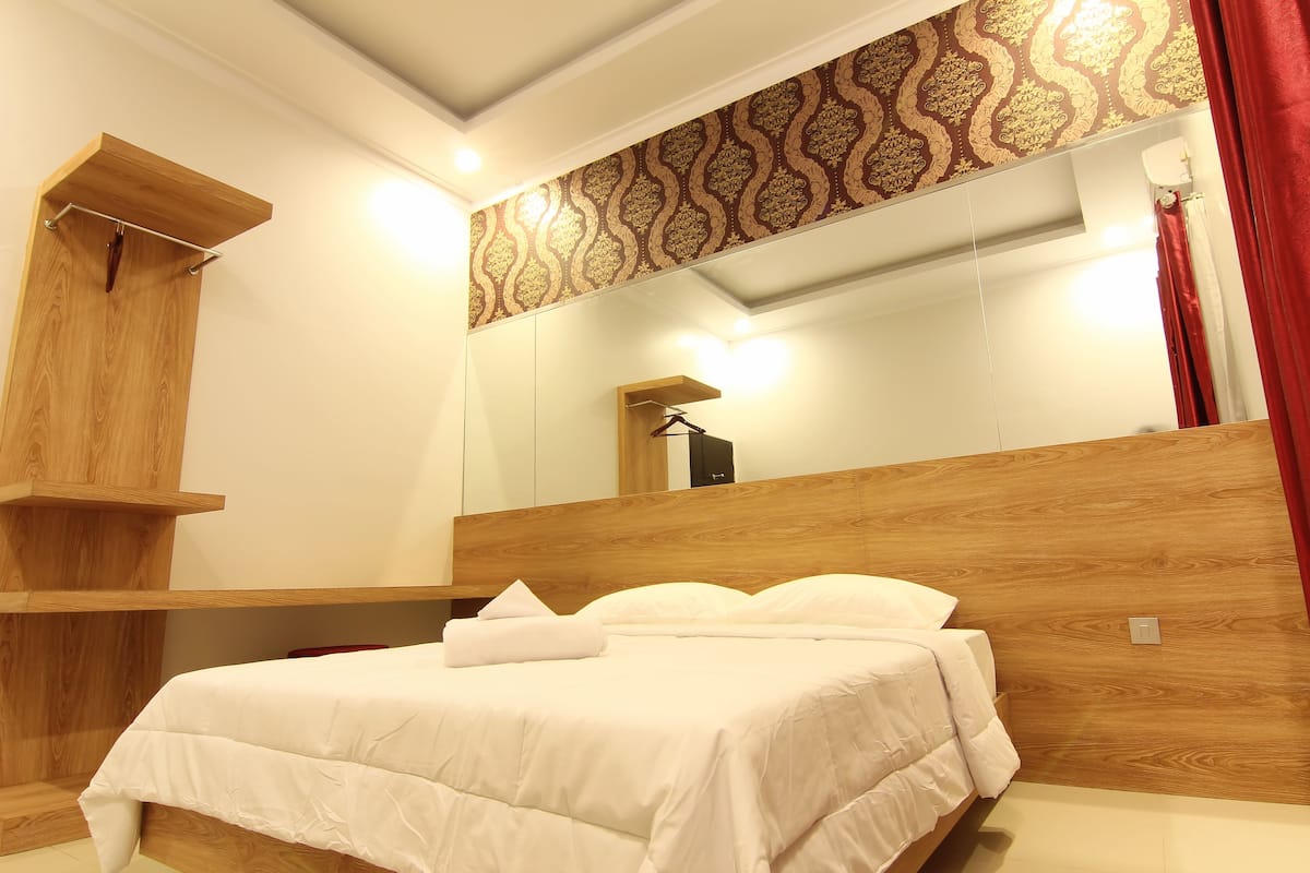 A modern bedroom with a wooden headboard, a large mirror, and a hanging coat rack.