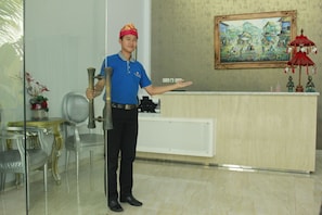 Un espace d’accueil d’hôtel comprenant un comptoir de réception, un réceptionniste et un tableau accroché au mur.