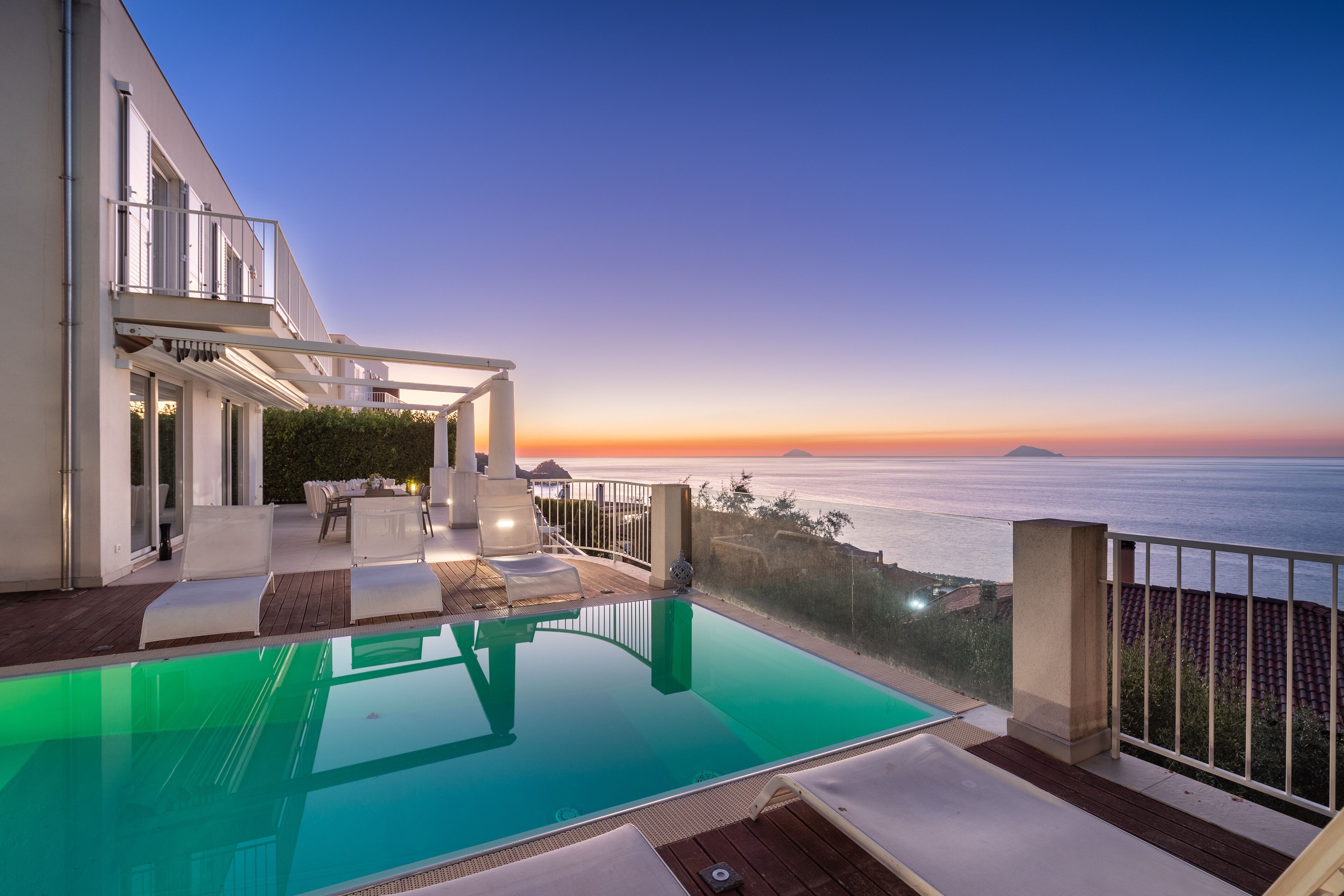 Une piscine à débordement moderne offrant une vue dégagée sur l’océan au coucher du soleil.