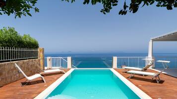 A pool area with a view of the ocean, surrounded by a wooden deck and white railings.
