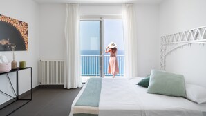 A bedroom with a bed, a nightstand, a radiator, and a view of the sea through a sliding door.