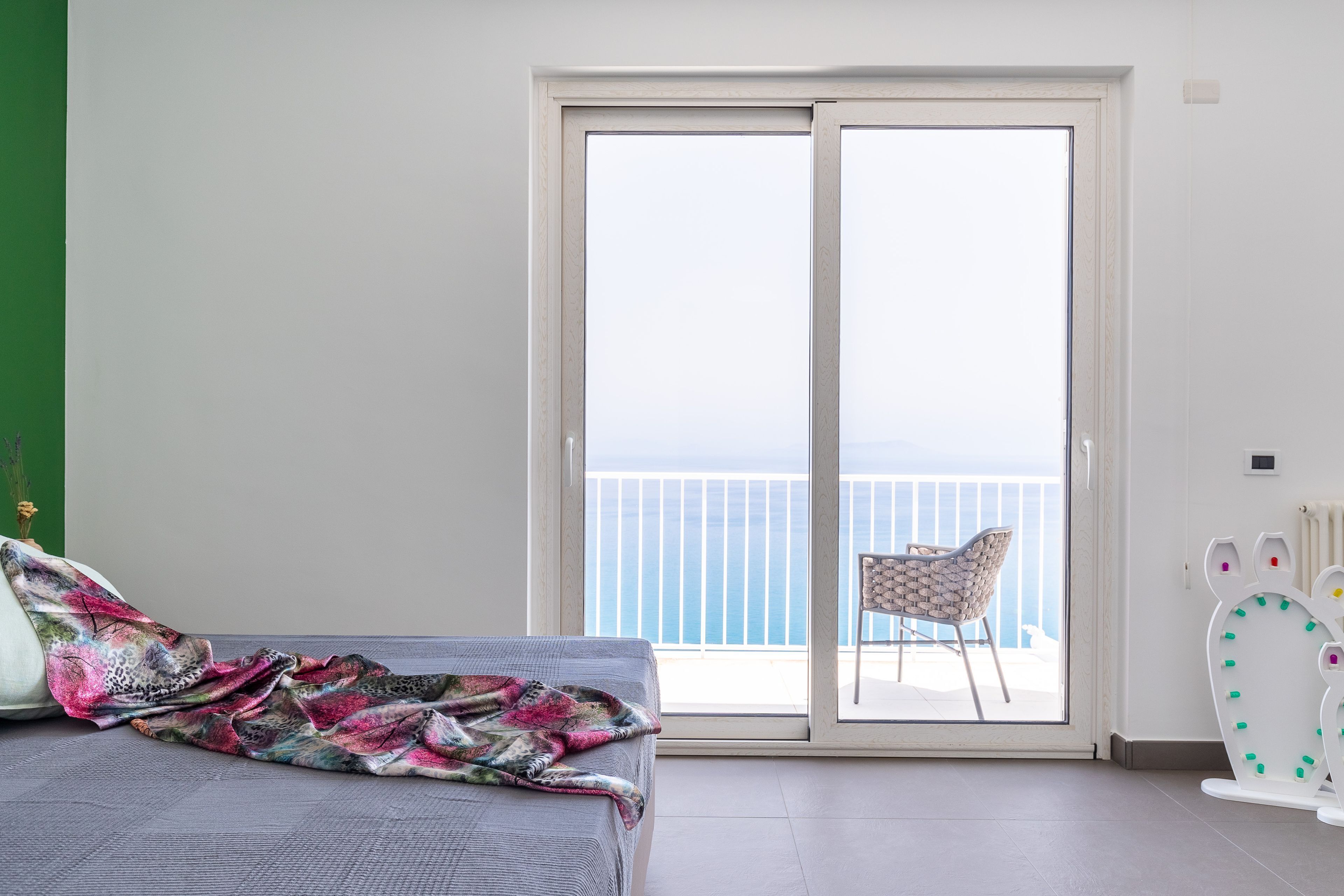 Un dormitorio con cama, una manta colorida, una silla y vistas al balcón.