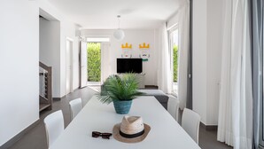 A modern dining area with a long table, chairs, a potted plant, and a hat.
