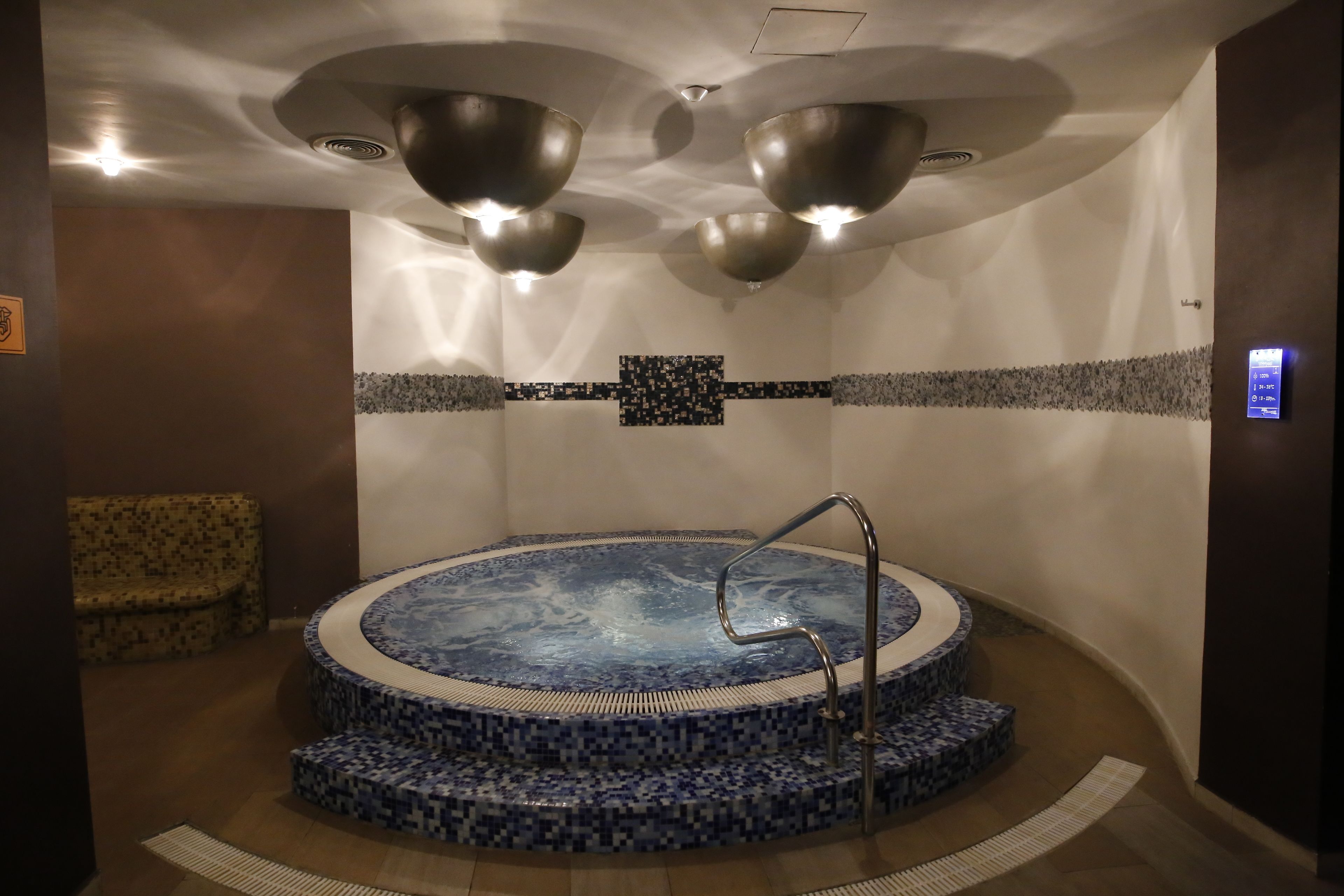 Un'area benessere con vasca idromassaggio, angolo relax e pannello di controllo a parete.