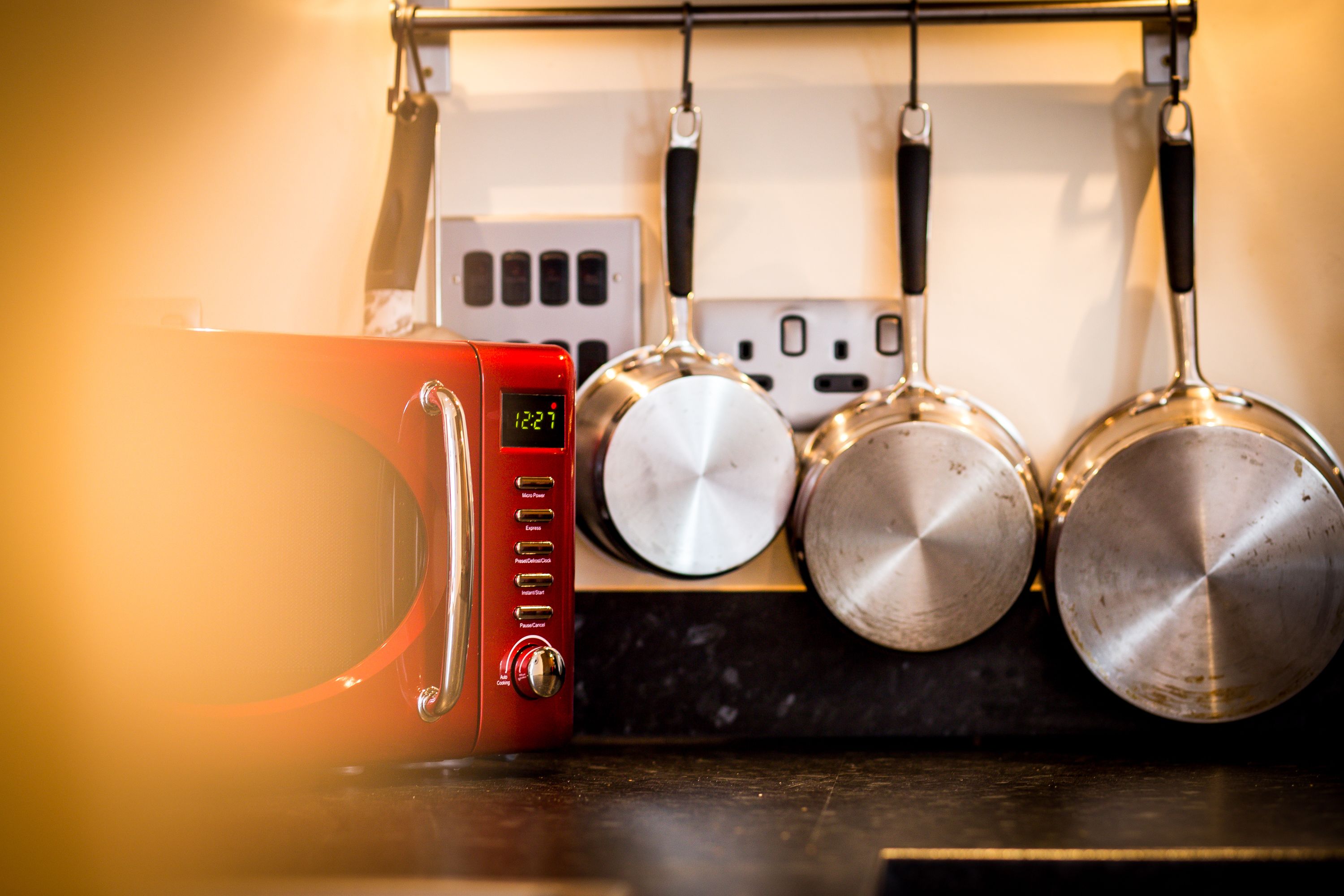 Une cuisine avec un four à micro-ondes rouge, une horloge numérique et trois casseroles suspendues à un étendoir.