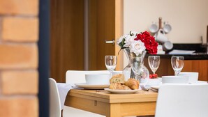 Uma mesa de jantar posta com pratos brancos, um vaso de vidro com flores, copos de vinho e croissants.